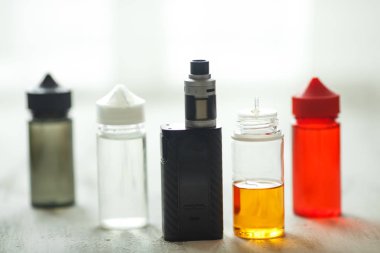 Vape nesneleri. Hafif ahşap bir masa üzerinde e-sıvı ile elektronik sigara ve kavanoz.