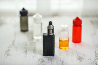 Vape nesneleri. Hafif ahşap bir masa üzerinde e-sıvı ile elektronik sigara ve kavanoz.