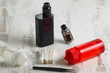 Vape nesneleri. Hafif ahşap bir masa üzerinde e-sıvı ile elektronik sigara ve kavanoz.