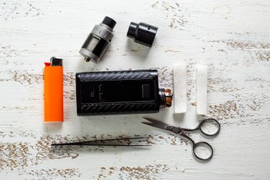 Vape nesneleri. Hafif ahşap bir masada elektronik sigara, pamuk, makas ve cımbız.