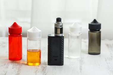 Vape nesneleri. Hafif ahşap bir masa üzerinde e-sıvı ile elektronik sigara ve kavanoz.