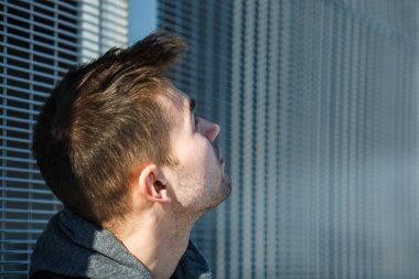 İlkbaharda güneşli bir günde sokakta metal bir kapının önünde siyah yelekli ciddi bir genç yakışıklı beyaz adamın portresi.