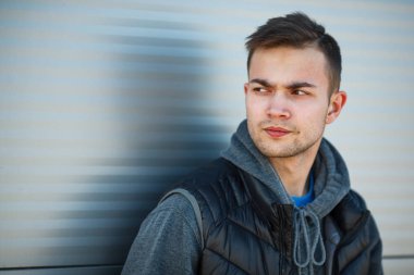 İlkbaharda sokakta çelik rulo kapılar karşısında siyah yelek li ciddi bir genç yakışıklı beyaz adam portresi.