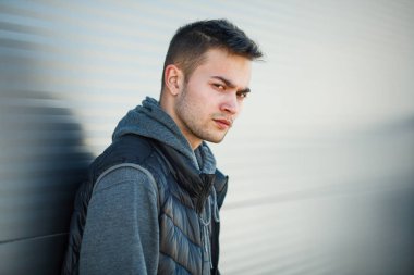 İlkbaharda sokakta çelik rulo kapılar karşısında siyah yelek li ciddi bir genç yakışıklı beyaz adam portresi.