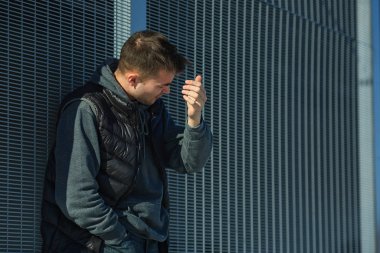 İlkbaharda güneşli bir günde sokakta metal bir kapının önünde siyah yelekli ciddi bir genç yakışıklı beyaz adamın portresi.