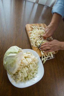 Kadın eller mutfakta masada tahta bir plaka üzerinde lahana kesti. Uygun beslenme.