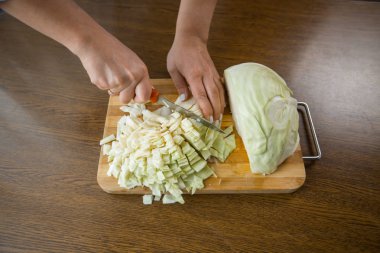 Kadın eller mutfakta masada tahta bir plaka üzerinde lahana kesti. Uygun beslenme.