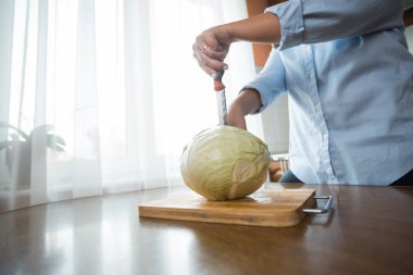 Kadın eller mutfakta masada tahta bir plaka üzerinde lahana kesti. Uygun beslenme.