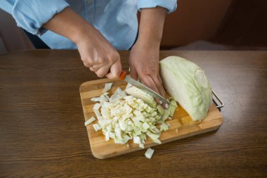 Kadın eller mutfakta masada tahta bir plaka üzerinde lahana kesti. Uygun beslenme.