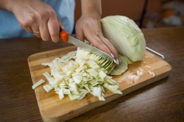 Kadın eller mutfakta masada tahta bir plaka üzerinde lahana kesti. Uygun beslenme.