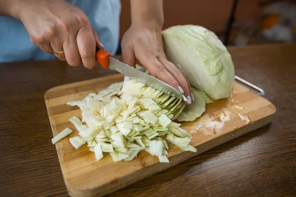 Kadın eller mutfakta masada tahta bir plaka üzerinde lahana kesti. Uygun beslenme.