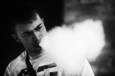 Vape adam. Genç yakışıklı beyaz adam kapalı portre vape barda bir elektronik sigara Buhar Puffs izin. Vaping süreci. Siyah ve beyaz. Kötü alışkanlık. Yakın çekim.