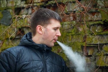 Vape adam. Siyah ceket sigara ve sonbahar eski yıkılan tuğla duvar yakın bir elektronik sigara buhar dışarı izin genç Kafkas Beyaz adam. Kötü alışkanlık. Vaping aktivitesi. Yaşam tarzı.