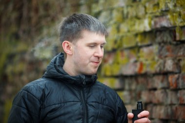 Vape adam. Siyah ceket sigara ve sonbahar eski yıkılan tuğla duvar yakın bir elektronik sigara buhar dışarı izin genç Kafkas Beyaz adam. Kötü alışkanlık. Vaping aktivitesi. Yaşam tarzı.