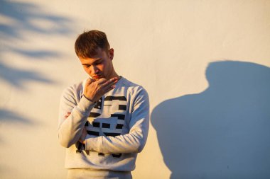 Gündelik giysiler içinde genç yakışıklı beyaz beyaz beyaz adam portresi sonbaharda gün batımında bir sokakta hafif bir duvarın önünde kalır.