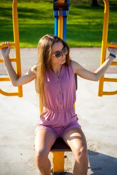 年轻的漂亮运动白种女孩穿着粉红色的连身衣和太阳镜在公园的街道运动场在夏天的一个阳光明媚的日子 街头运动场健身 — 图库照片