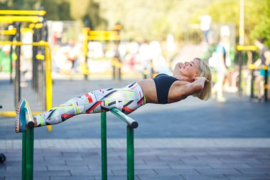 Eşofmanlı güzel olgun kadın yaz aylarında güneşli bir günde parkta sokak sporları zemin üzerinde egzersizler yapar. Sokak sporları zemininde fitness.