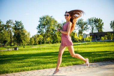 Genç. Pembe tulum ve güneş gözlüğü genç oldukça sportif kafkas kız yaz aylarında güneşli bir günde parkta atlama.