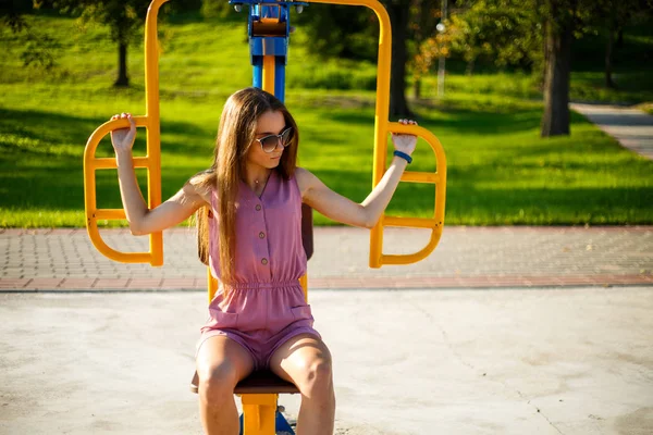 Yaz aylarında güneşli bir günde parkta sokak sporları alanında pembe tulum ve güneş gözlüğü genç oldukça sportif kafkas kız. Sokak sporları zemininde fitness.