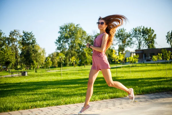 Genç. Pembe tulum ve güneş gözlüğü genç oldukça sportif kafkas kız yaz aylarında güneşli bir günde parkta atlama.