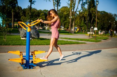 Yaz aylarında güneşli bir günde parkta sokak sporları alanında pembe tulum ve güneş gözlüğü genç oldukça sportif kafkas kız. Sokak sporları zemininde fitness.