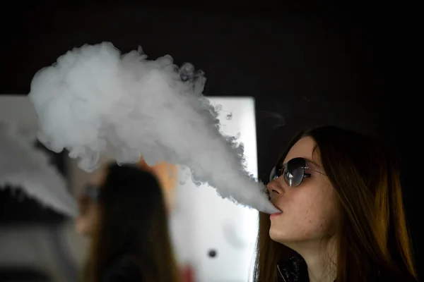 Sorunlu cildi olan Vape genç. Güneş gözlüğü genç sevimli kız portresi barda ayna karşısında elektronik sigara içen. Kötü alışkanlık. Vaping aktivitesi. Karanlık atış.