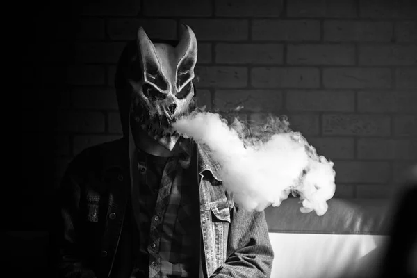 Şeytan maskeli vape adam ve kapalı bir elektronik sigara içen bir başlık. Buhar puffs. Sağlık için zararlı kötü alışkanlık. Vaping aktivitesi. Siyah beyaz.