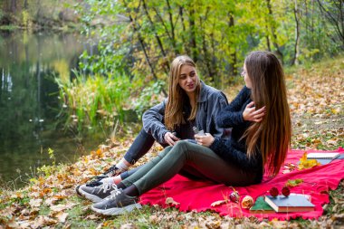 Vape lgbt teenagers. Bisexual lesbian young caucasian teenage girls in casual clothes vape electronic cigarette near the river on the street in the park in the autumn evening. Bad habit.