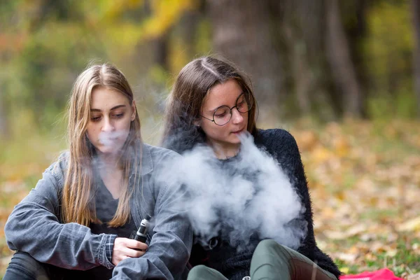 Vape lgbt gençleri. Biseksüel lezbiyen, beyaz, günlük kıyafetler giyen genç kızlar sonbahar akşamı parkta sokakta elektronik sigara yakarlar. Kötü alışkanlık..