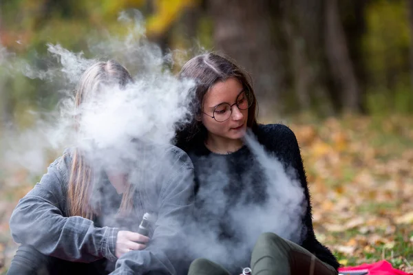 Vape lgbt gençleri. Biseksüel lezbiyen, beyaz, günlük kıyafetler giyen genç kızlar sonbahar akşamı parkta sokakta elektronik sigara yakarlar. Kötü alışkanlık..