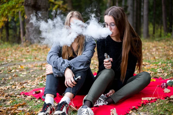 Vape lgbt gençleri. Biseksüel lezbiyen, beyaz, günlük kıyafetler giyen genç kızlar sonbahar akşamı parkta sokakta elektronik sigara yakarlar. Kötü alışkanlık..