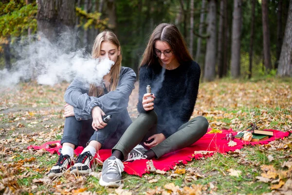 Vape lgbt gençleri. Biseksüel lezbiyen, beyaz, günlük kıyafetler giyen genç kızlar sonbahar akşamı parkta sokakta elektronik sigara yakarlar. Kötü alışkanlık..