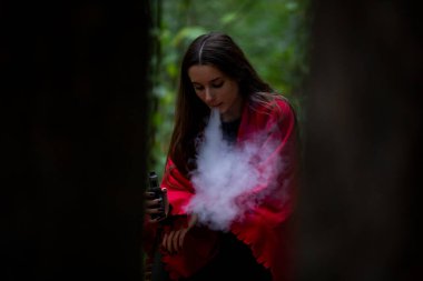 Genç bir erkek. Genç, beyaz, beyaz, günlük kıyafetler içinde, kırmızı ekose kumaşla kaplı genç bir kız sonbahar akşamları, karanlık bir ormanda sokakta elektronik bir sigara yakıyor. Kötü alışkanlık..