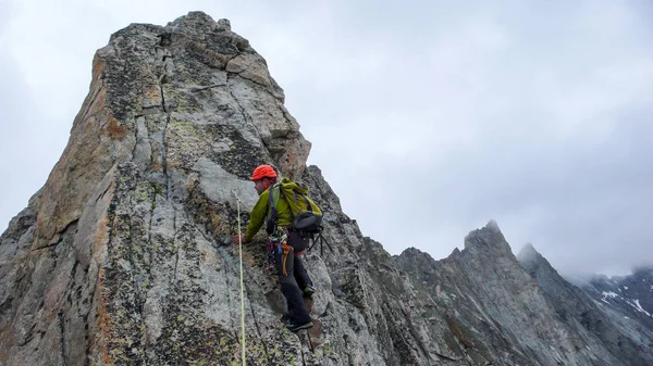 male mountain guide lead climbing on an exposed granite ridge in the Alps