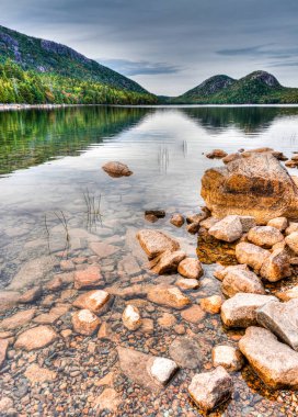 woodlands yansıma ve ön planda kırmızı kayalar ile güzel dağ Gölü
