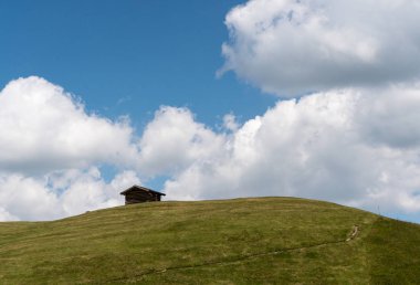 çimenli alp hill ve ridge mavi gökyüzü ile İsviçre Alpleri'nde beyaz bulutlar altında küçük ahşap kulübe