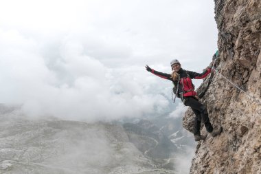 genç çekici kadın üniversite öğrencisi bir dikey ve maruz rock yüzündeki Via Ferrata gülümseyen ve sallayarak ve bir barış işareti yapma tırmanıyor