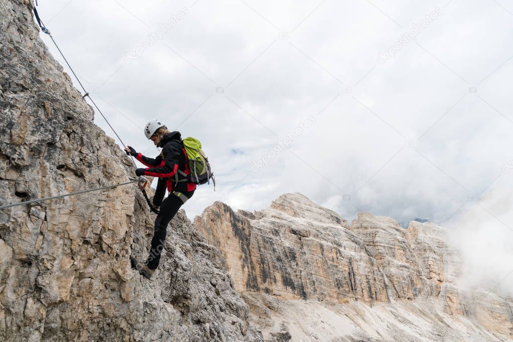 young attractive female university student on a vertical and exposed rock face climbs a Via Ferrata in Alta Badia in the South Tyrol
