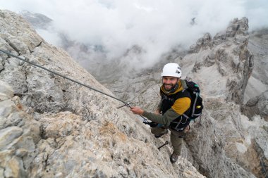 Genç erkek tırmanıcı dik ve çıplak kaya yüzeyinde Via Ferrata 'ya tırmanıyor.
