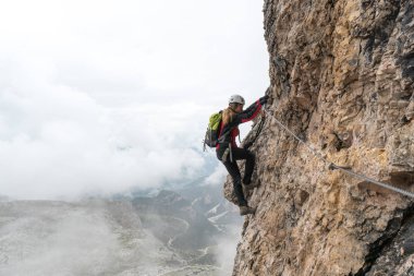 Genç bayan tırmanıcı dik ve açıkta bir kaya yüzeyinde Via Ferrata 'ya tırmanıyor.