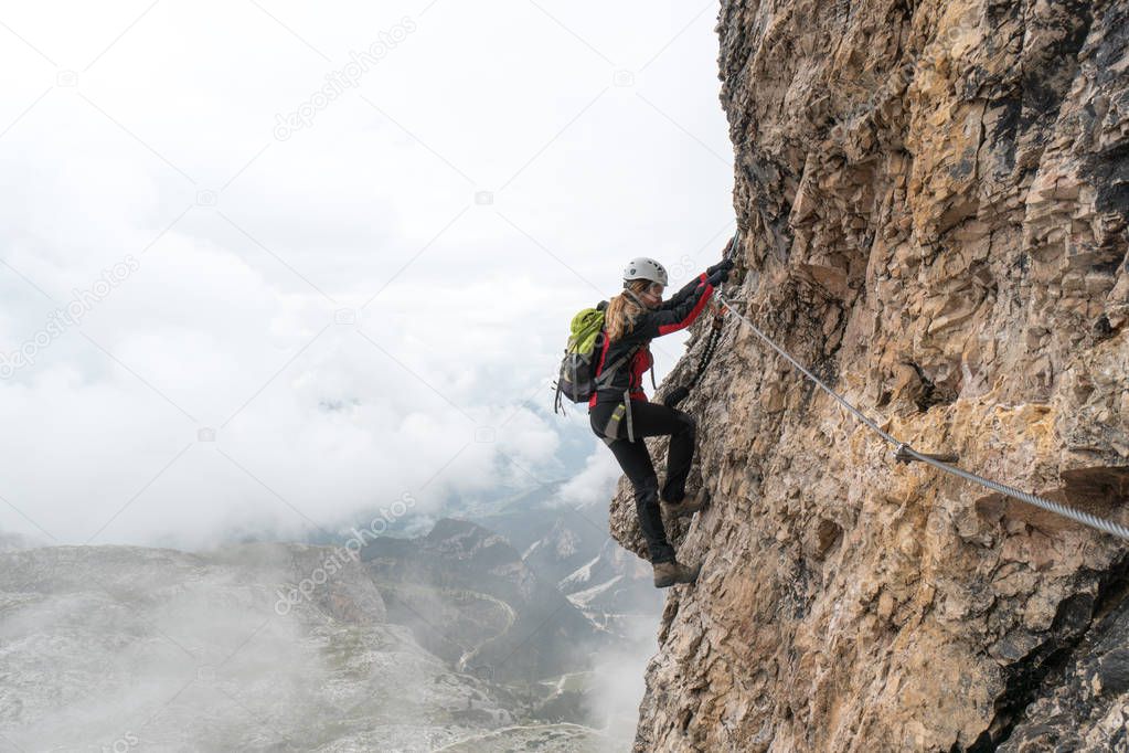 young female climber on a vertical and exposed rock face climbing a Via Ferrata