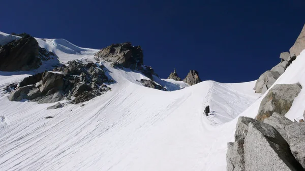 mountain guide and client climbing a steep snow ridge on a north face in the Alps above Chamonix