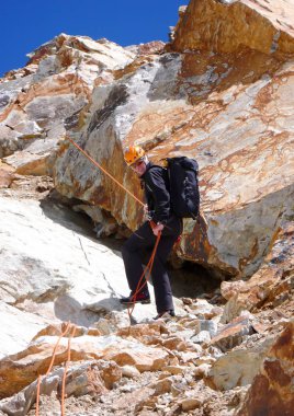 yüksek tepeler ve açık mavi gökyüzü altında İsviçre Alpleri dağlarında kırmızı kayalar üzerinde aşağı rappelling dağcı