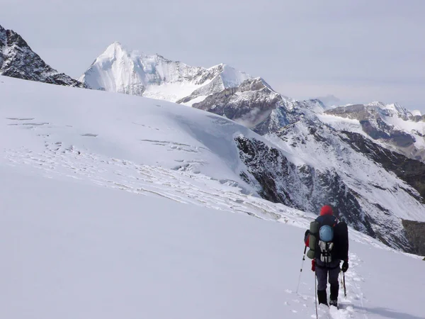 single male mountain climber carrying a lot of climbing equipment in the Mischabel mountain range in the Swiss Alps above Saas Fee