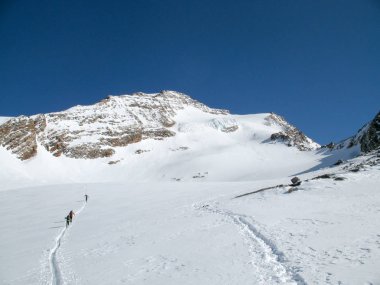 Kışın büyük bir dağ buzul mavi gökyüzü altında uzak dağ tepe doğru yola geçiş birkaç backcountry kayakçı