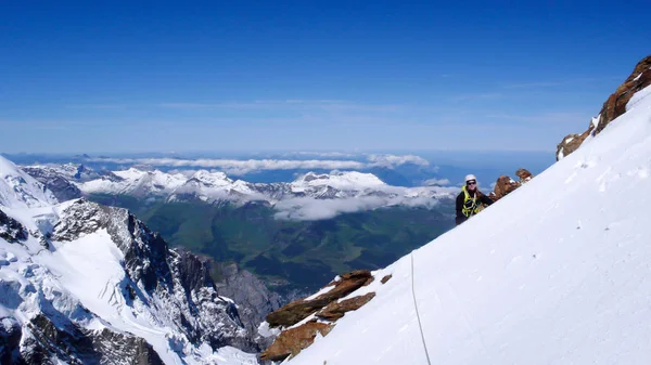 female mountain climber on a steep snow and ice mountain side with a fantastic view of the surrounding mountain landscape and mountain peaks on a beautiful summer day