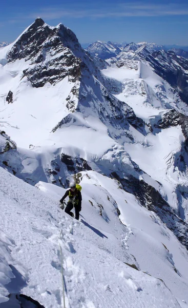 female mountain climber on a steep snow and ice mountain side with a fantastic view of the surrounding mountain landscape and mountain peaks on a beautiful summer day