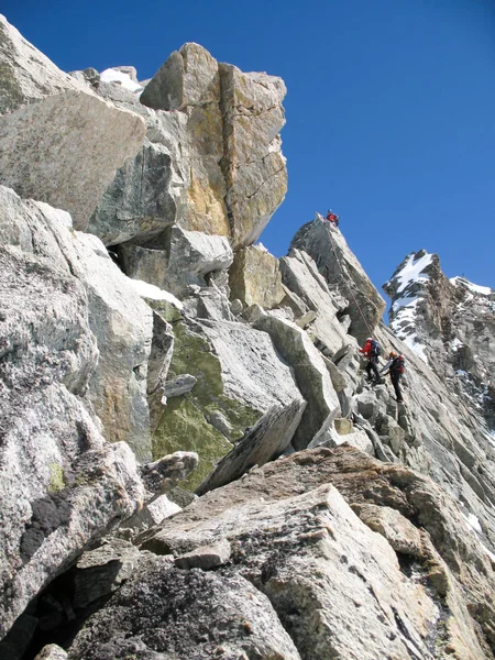 jagged rock and snow mountain ridge with three mountain climbers in the background