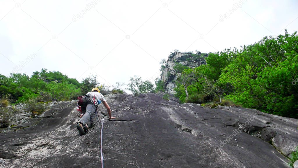 male rock climber on a steep climbing route in southern Switzerland on a hot summer day on black gneiss rock