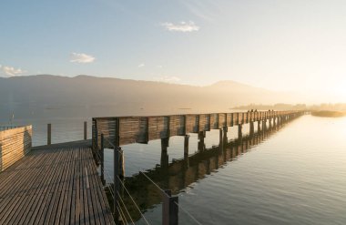 Uzun ahşap tahta İskelesi ile bir dağ manzara siluet arka planda altın akşam ışık su üzerinde